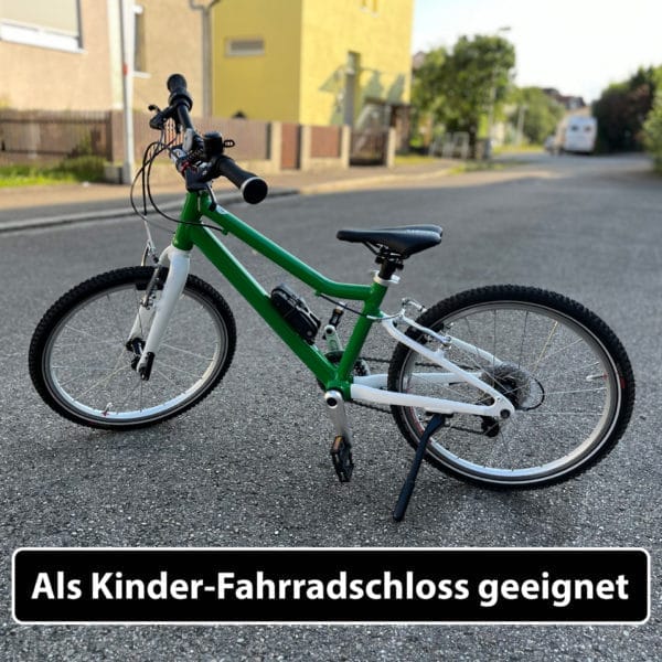 Ein grün-weißes Kinderfahrrad, gesichert mit dem Leichtes & kleines Faltschloss "Zürich", mit der Aufschrift "Als Kinder-Fahrradschloss geeignet".