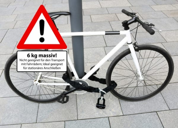 Ein weißes Fahrrad ist mit dem massiven Sicherheits-Motorradschloss "Alcatraz" an einem Pfahl befestigt; ein deutsches Warnschild weist auf das Gewicht und den Verwendungszweck des Schlosses hin.