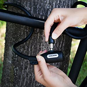 Person sichert ein Fahrrad mit dem Langes Kabelschloss mit Zuklick-Mechanismus "Paris" an einem Baumstamm und einer Metallstange.