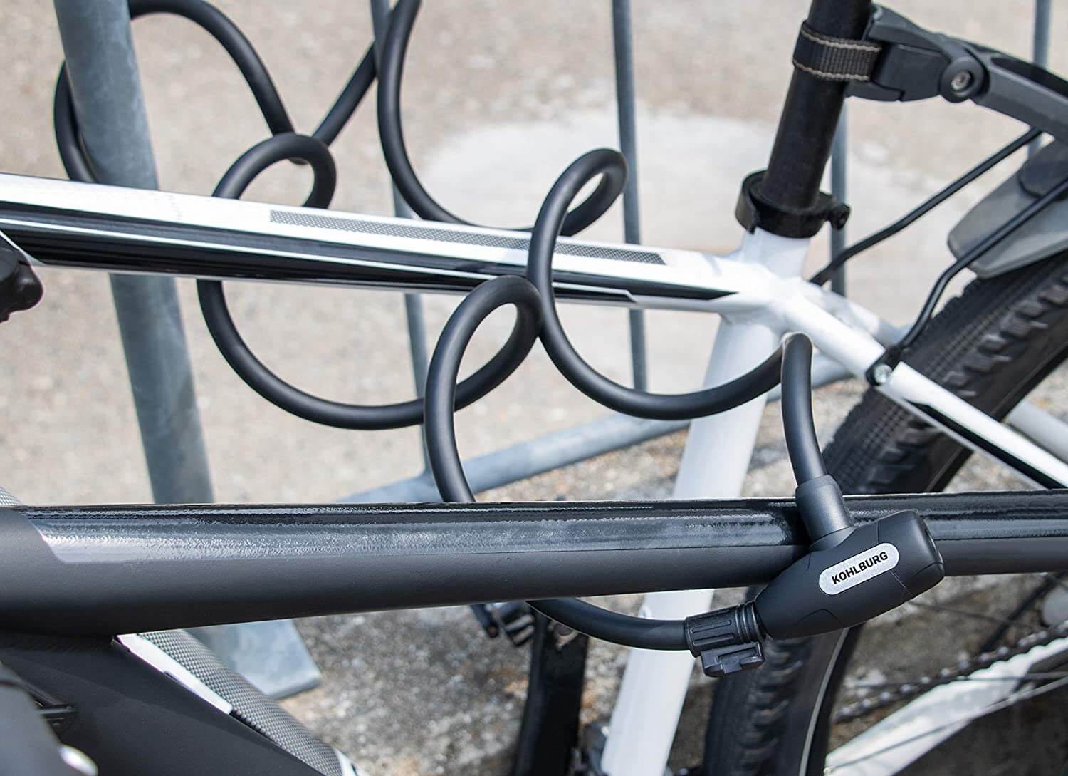 Das Langes Kabelschloss mit Zuklick-Mechanismus "Paris" sichert einen weißen Fahrradrahmen an einem Metall-Fahrradständer im Freien.