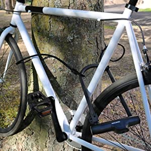 Ein weißes Fahrrad ist an einem Baum in einem sonnigen Park mit dem Sicherheits-Bügelschloss "Novosibirsk" inkl. Sicherheitskabel befestigt. Sicherheitskabel.
