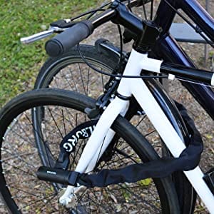 Zwei Fahrräder zusammen mit dem extra-langen Sicherheits-Kettenschloss "Helsinki" auf einem Schotterweg gesichert, Gras in der Nähe.