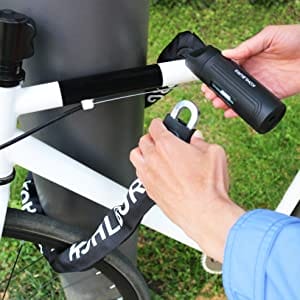 Eine Person schließt ein weißes Fahrrad im Freien mit dem extra-langen Sicherheits-Kettenschloss "Helsinki" an einem Pfosten ab.