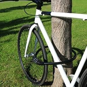 Ein weißes Fahrrad, das an einem Baum auf einer Wiese mit dem Langes massives Kabelschloss mit Zahlenkombination "Bordeaux" befestigt ist.
