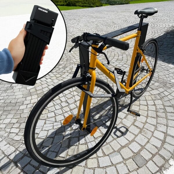 Gelbes Fahrrad auf einem Steinweg; in der Mitte eine Hand, die das Sicherheitsfaltschloss "Catania" hält.